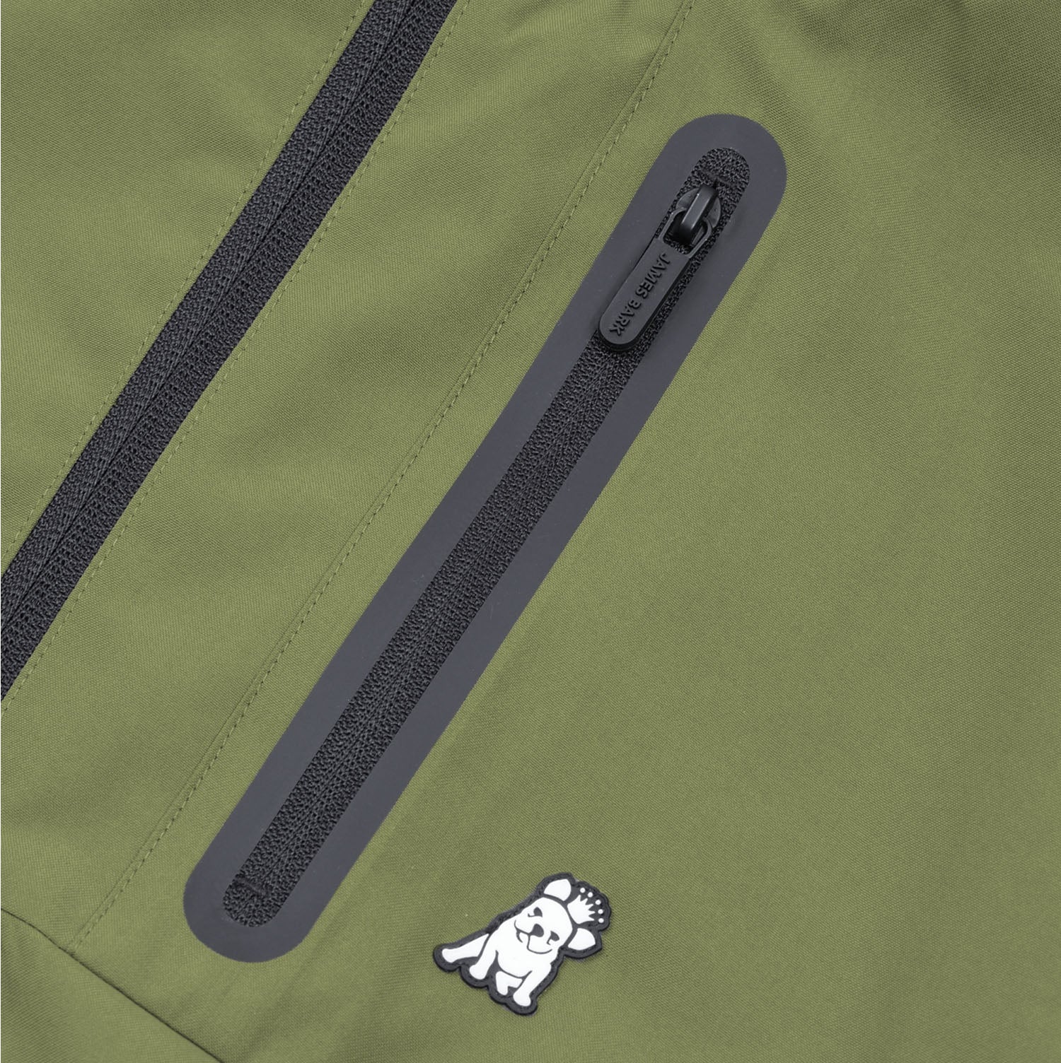 Close-up of the side pocket zipper on the green jacket with the James Bark logo.