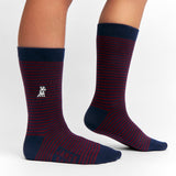 Close-up view of navy and burgundy striped socks being worn, showing the small embroidered dog logo and solid navy details on the heel, toe, and cuff.