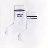 Pair of white socks with black stripes near the cuff and "James Bark" text logo in black, displayed flat.