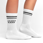 White socks with black stripes and "James Bark" logo, shown worn to display the design and fit on the legs.