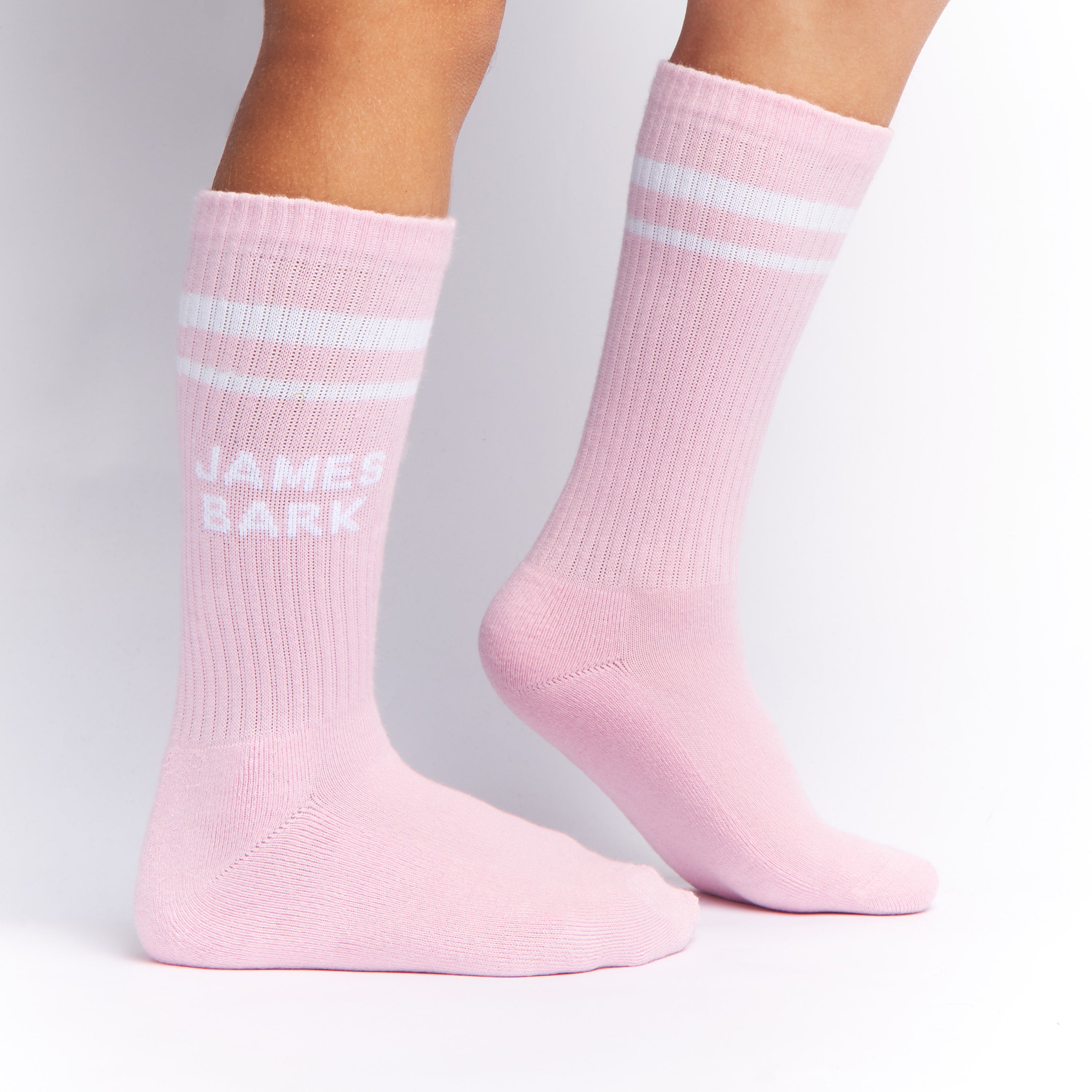 Pink socks with white stripes and "James Bark" logo, shown worn to display the design and fit on the legs.