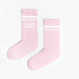 A pair of pink mid-calf socks with two white stripes at the top and the text 'JAMES BARK' printed in white near the ankle. The socks are laid flat on a white surface.