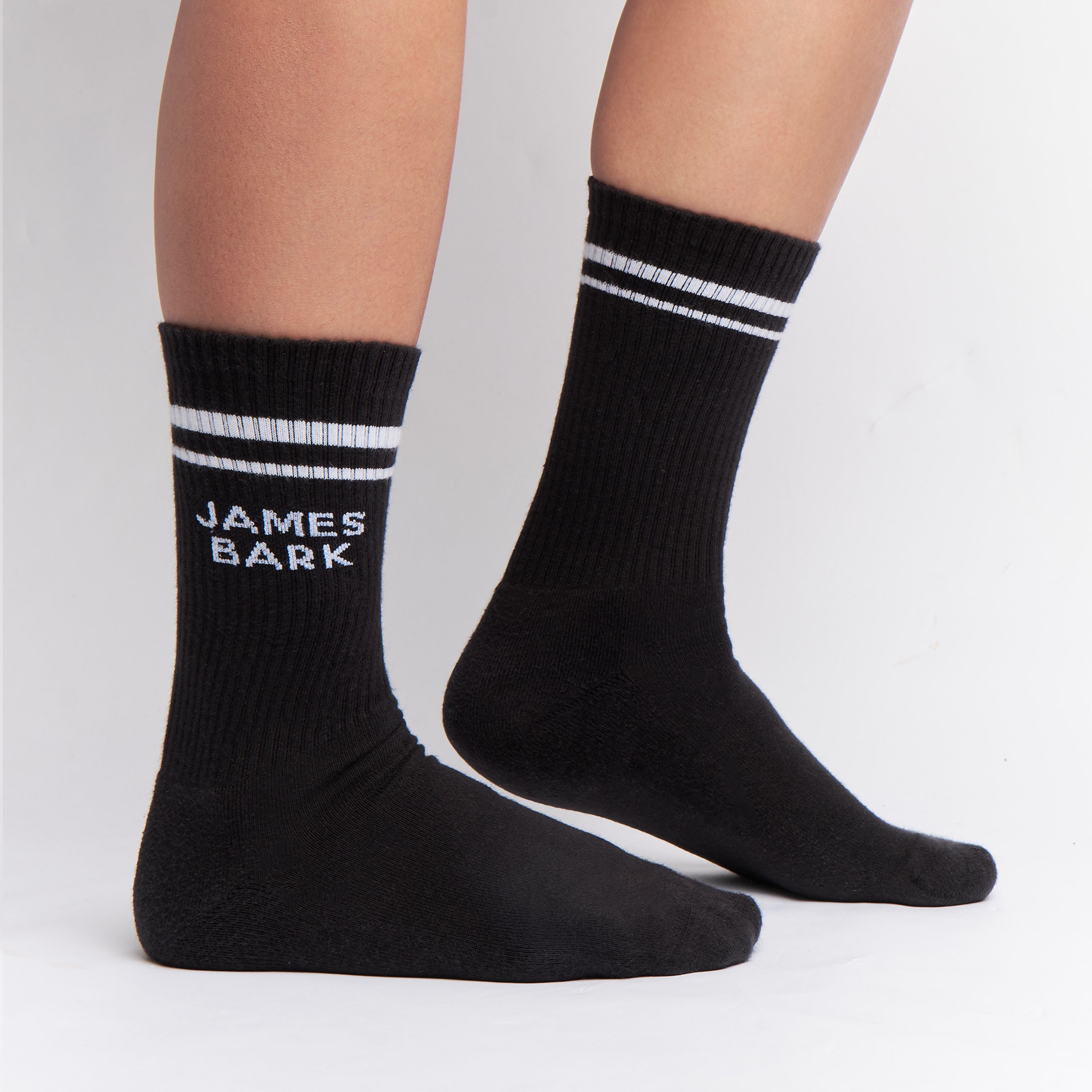 Black mid-calf socks with two white stripes at the top and the text 'JAMES BARK' in white on the ankle, shown worn on a person’s feet.