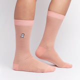 Light pink mid-calf socks with subtle stripes, a solid pink cuff, heel, and toe, featuring a small dog graphic near the ankle, shown worn on a person’s feet.