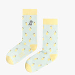 A pair of light blue mid-calf socks with a yellow cuff, heel, and toe, featuring a pattern of lemons and a small dog graphic near the ankle. The text 'JAMES BARK' is printed in yellow near the toe. The socks are laid flat on a white surface.