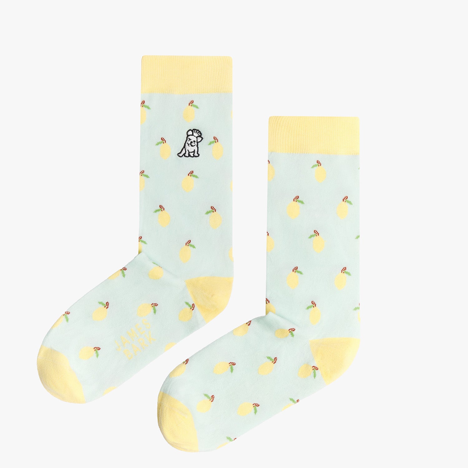 A pair of light blue mid-calf socks with a yellow cuff, heel, and toe, featuring a pattern of lemons and a small dog graphic near the ankle. The text 'JAMES BARK' is printed in yellow near the toe. The socks are laid flat on a white surface.