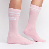 Pink mid-calf socks with two white stripes at the top and the text 'JAMES BARK' in white on the ankle, shown worn on a person’s feet.