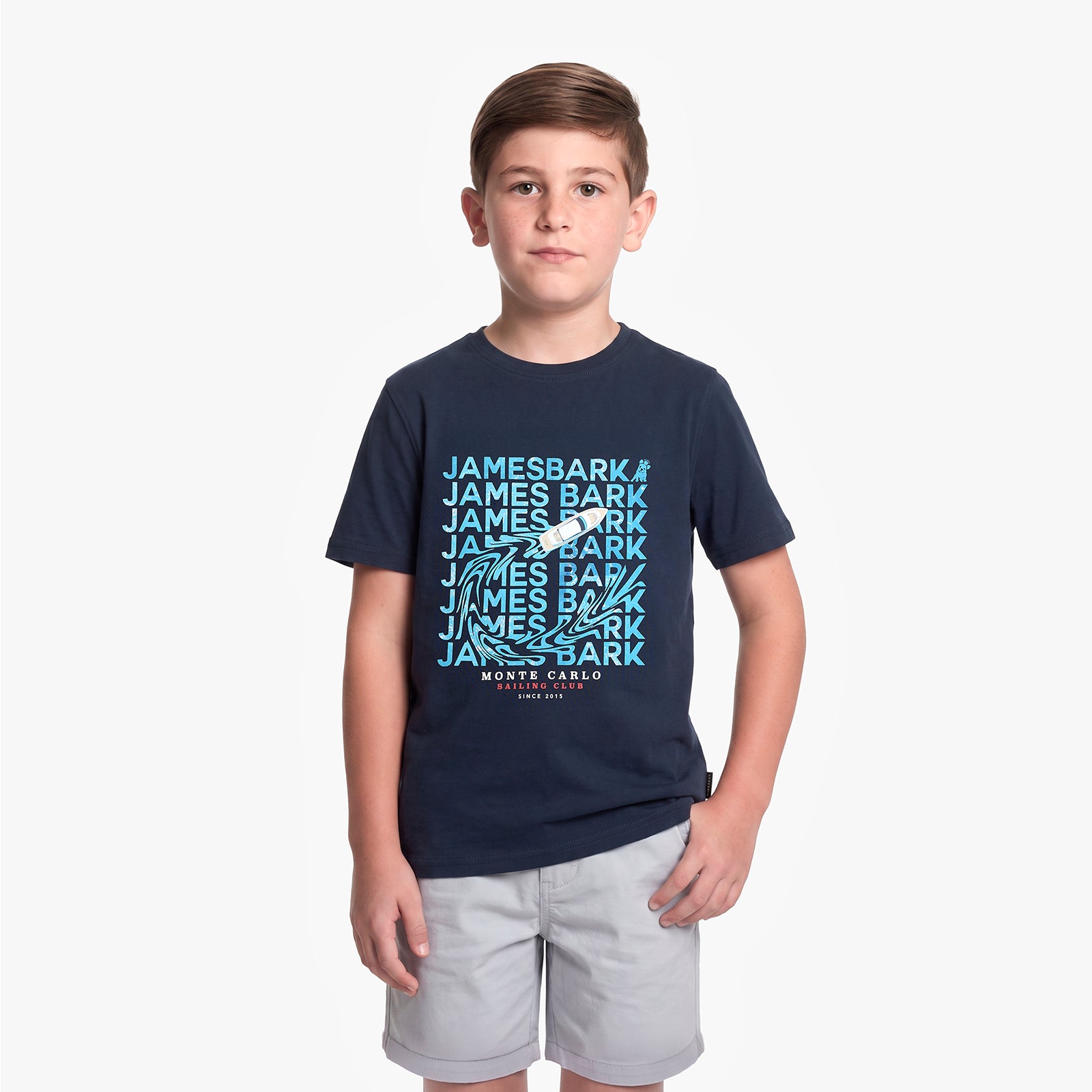 A young boy modeling a navy blue T-shirt with a light blue and white 'James Bark' graphic print on the front