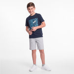 A young boy wearing a navy blue T-shirt with a light blue and white 'JAMES BARK' graphic, paired with light gray shorts and white sneakers