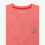 Close-up of the chest area of the pink t-shirt: A detailed view showing the small embroidered dog logo in white and black on the left chest, along with the inner label featuring branding and care information.