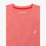 Close-up of the salmon pink t-shirt, showing the crew neckline and a small embroidered animal logo on the left chest.