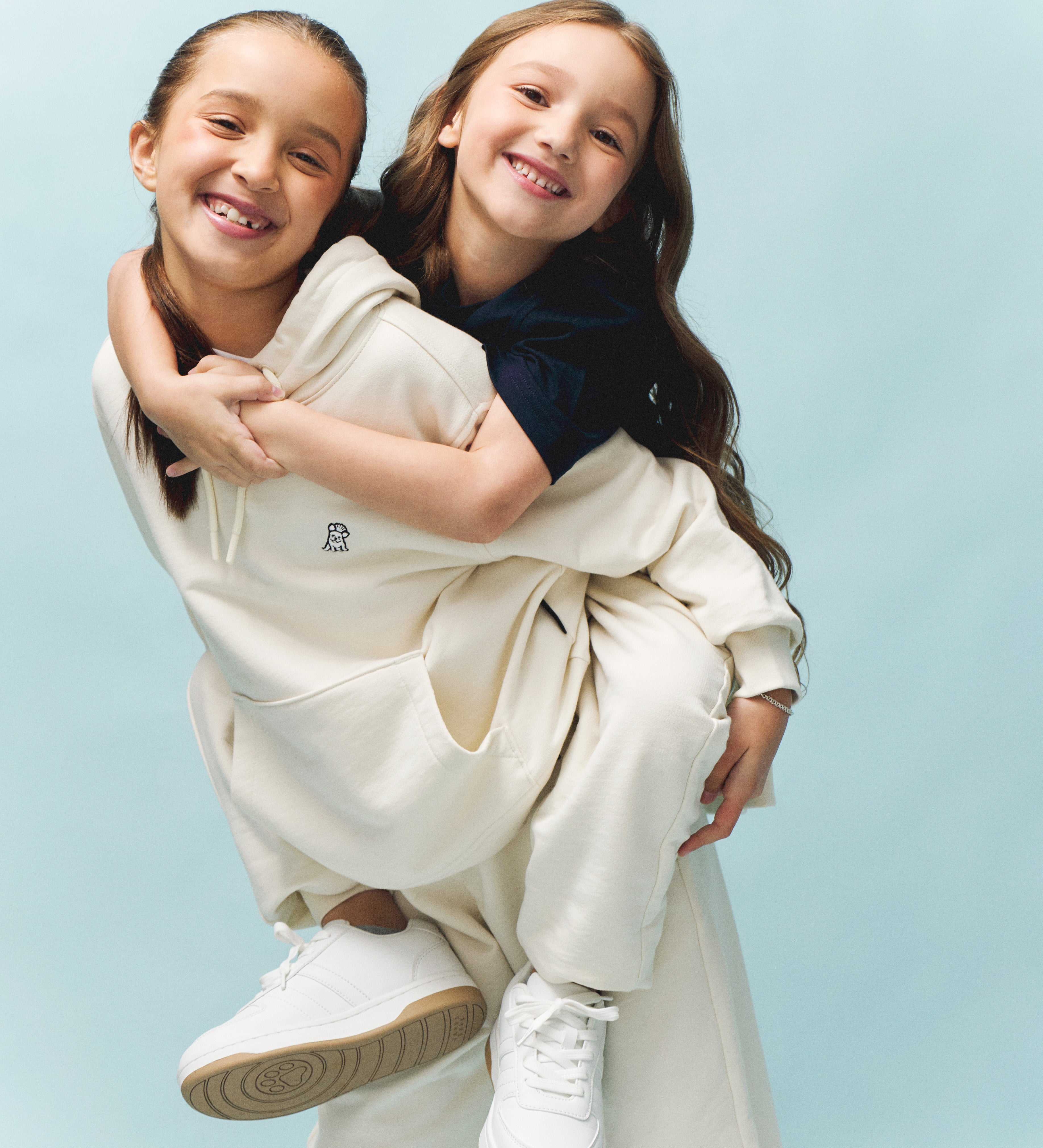 Two children hugging, wearing white French terry sets against a light blue background
