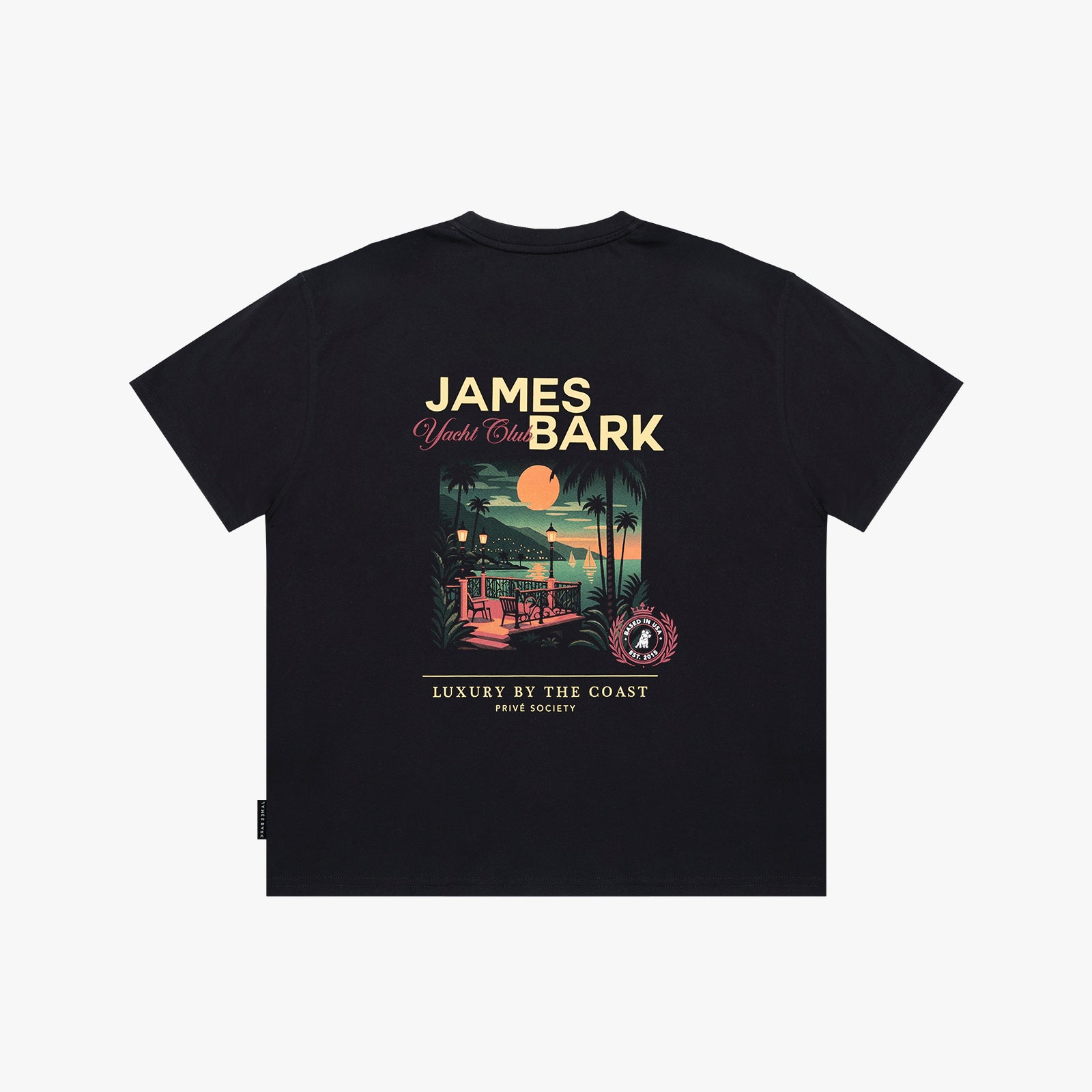 A black T-shirt shown flat, featuring a large graphic print on the back with the text 'JAMES BARK' and 'Luxury by the Coast'. The graphic depicts a sunset beach scene with a pool and palm trees.