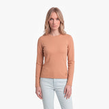 Woman wearing a tan long-sleeve shirt and light blue jeans on a white background