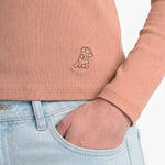 Person wearing a pink ribbed sweater with a logo and light blue jeans.