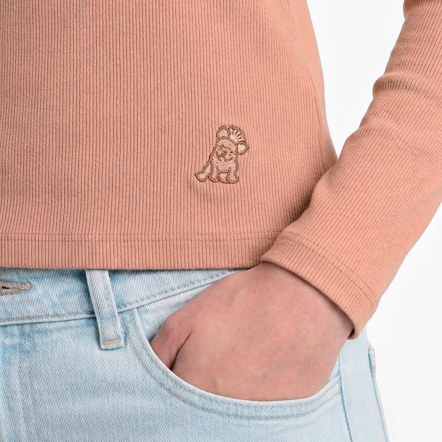 Person wearing a pink ribbed sweater with a logo and light blue jeans.