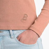 Person wearing a pink ribbed sweater with a logo and light blue jeans.