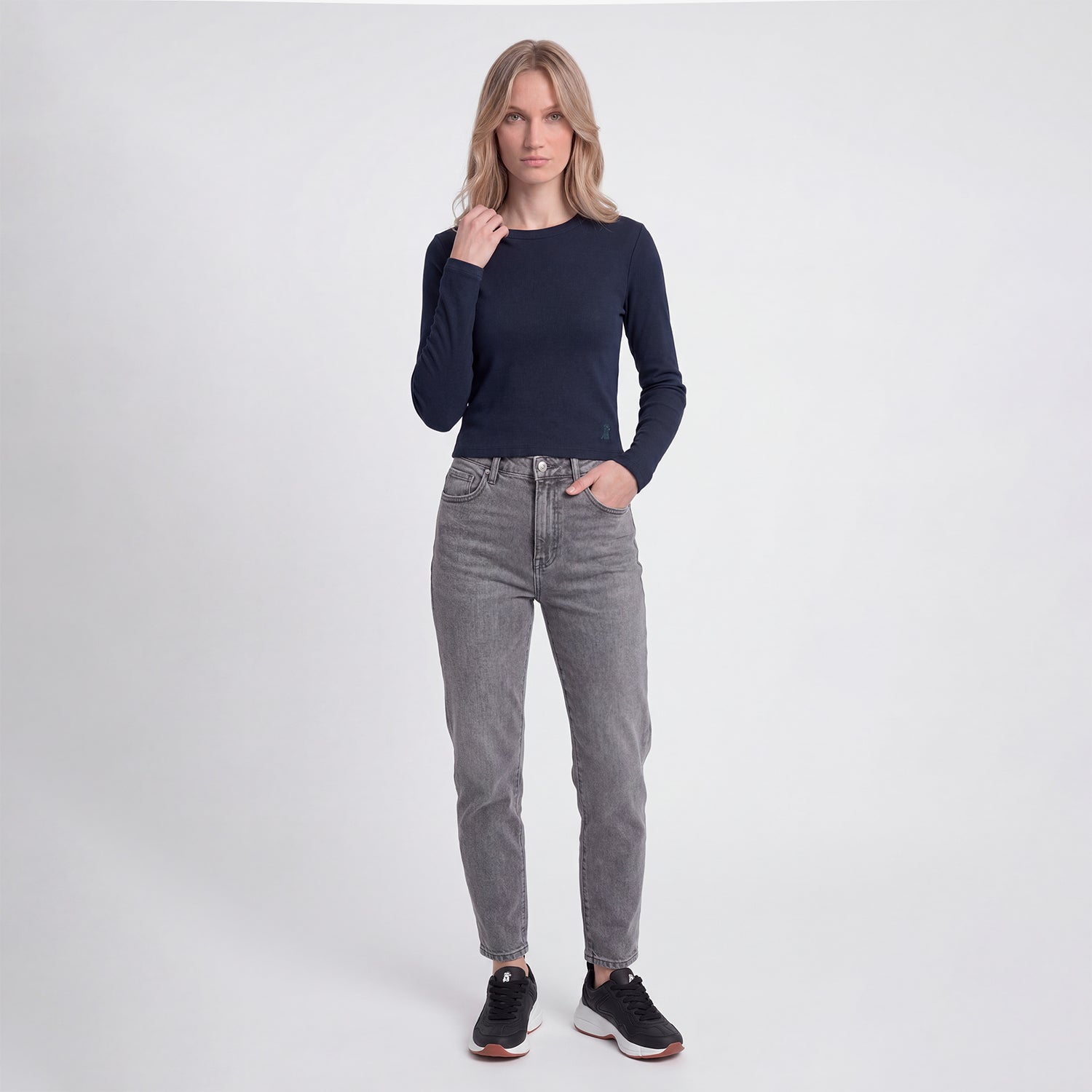 Woman wearing a navy long-sleeve top and gray jeans on a white background