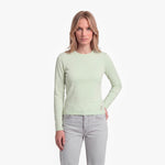 Woman wearing a light green long-sleeve shirt and light gray jeans on a white background