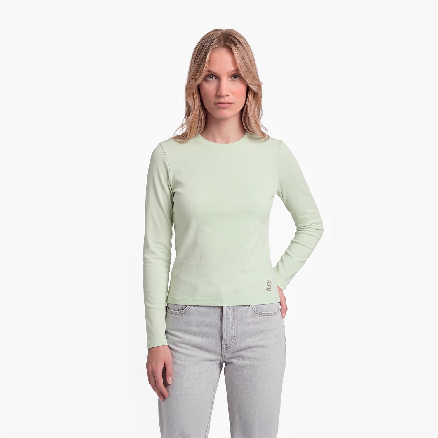 Woman wearing a light green long-sleeve shirt and light gray jeans on a white background