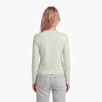 Woman wearing a light green long-sleeve shirt and light gray jeans on a white background