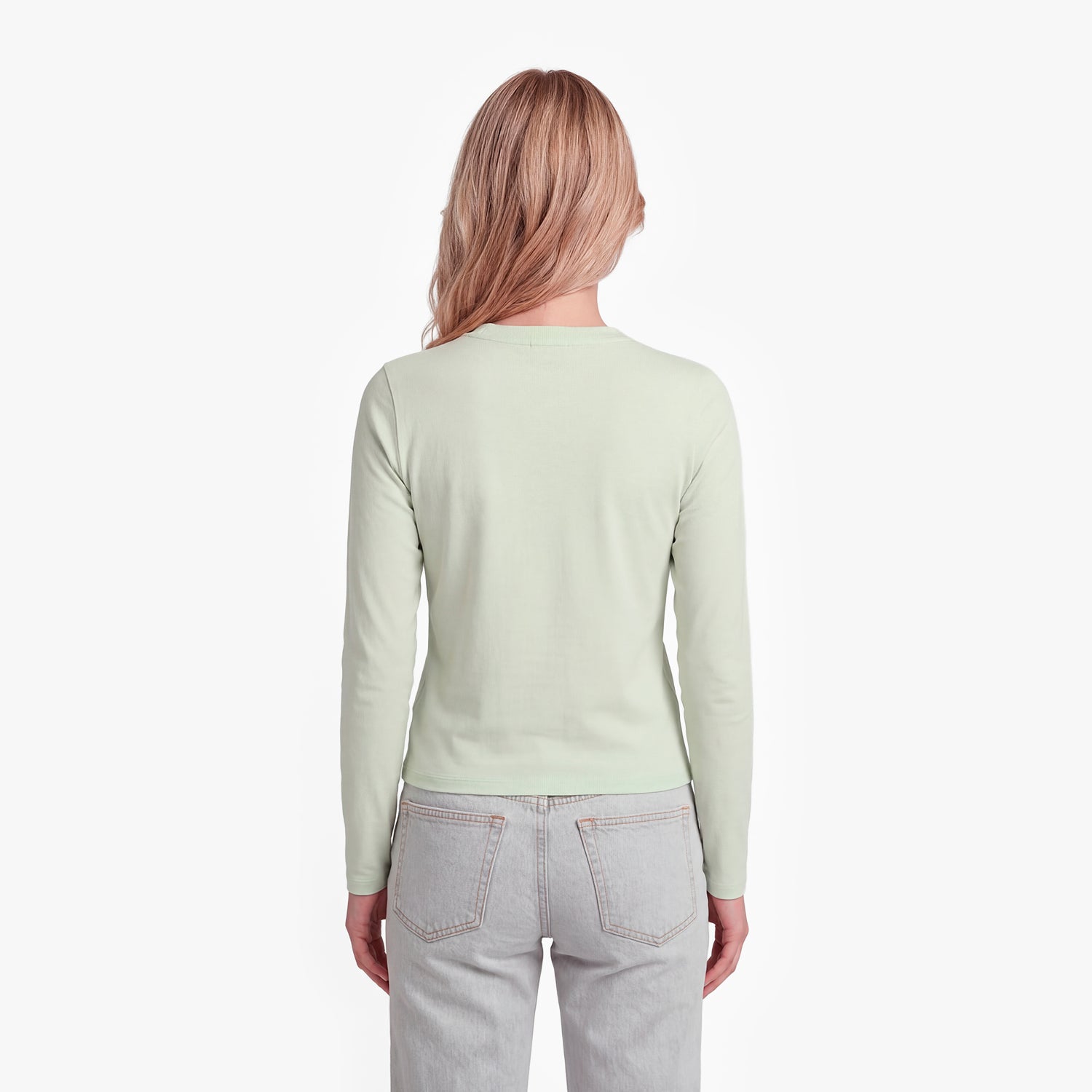 Woman wearing a light green long-sleeve shirt and light gray jeans on a white background