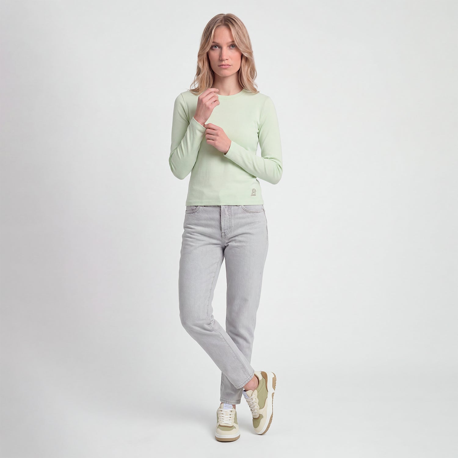 Woman wearing a light green sweater and gray jeans on a white background