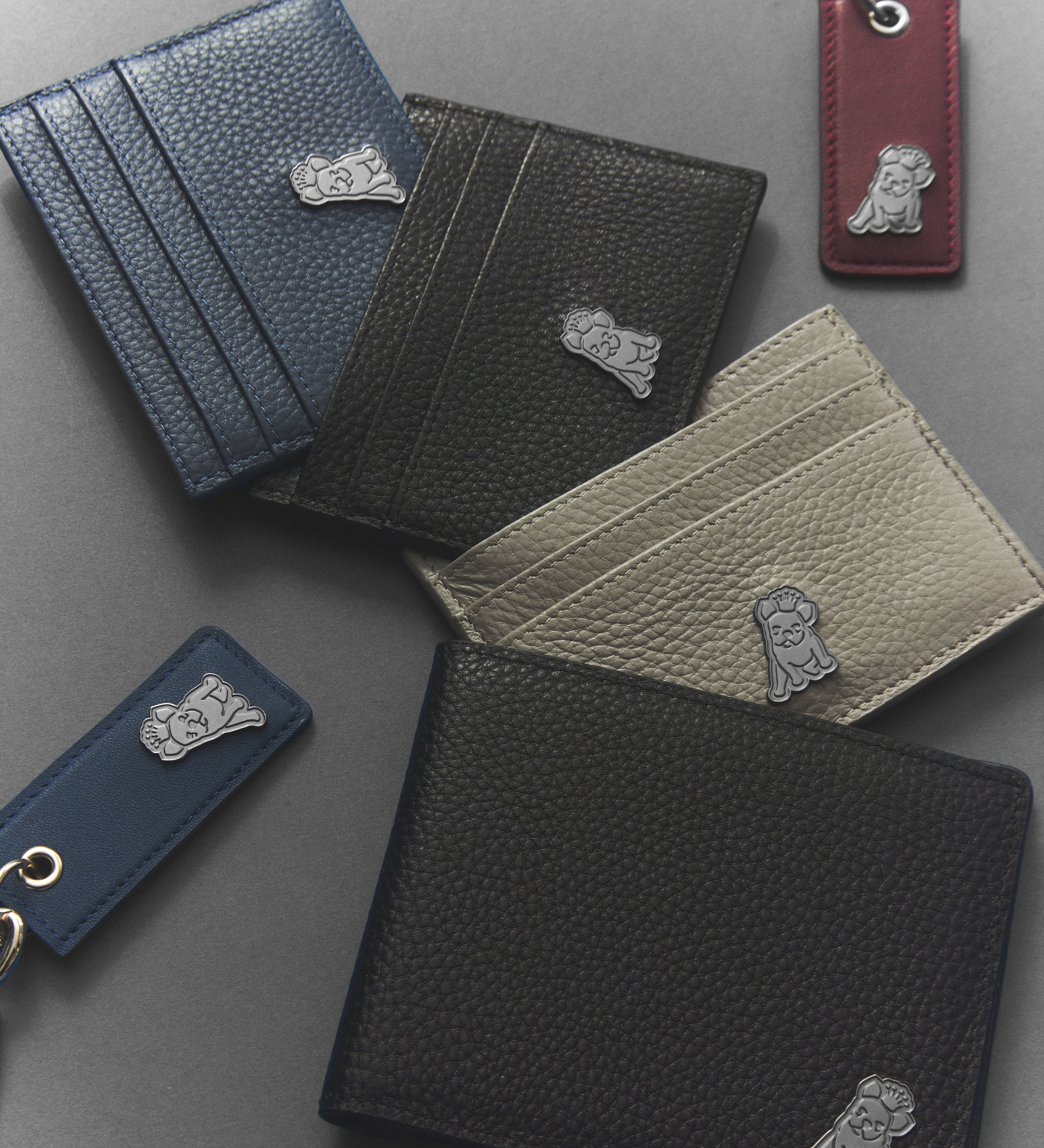 Collection of leather wallets and keychains with a brand logo on a gray surface