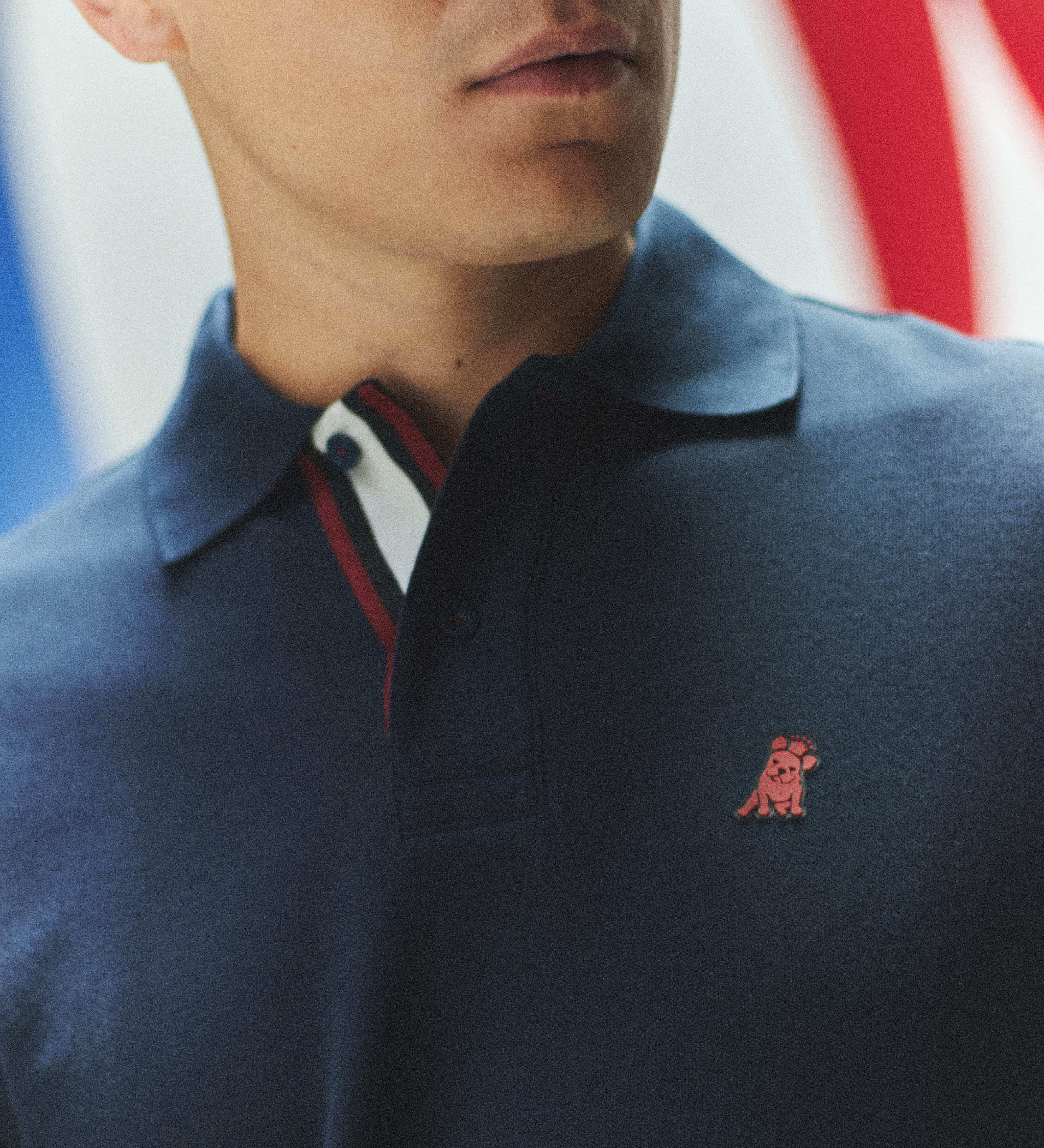 Man wearing a navy blue polo shirt with a red logo, blurred background