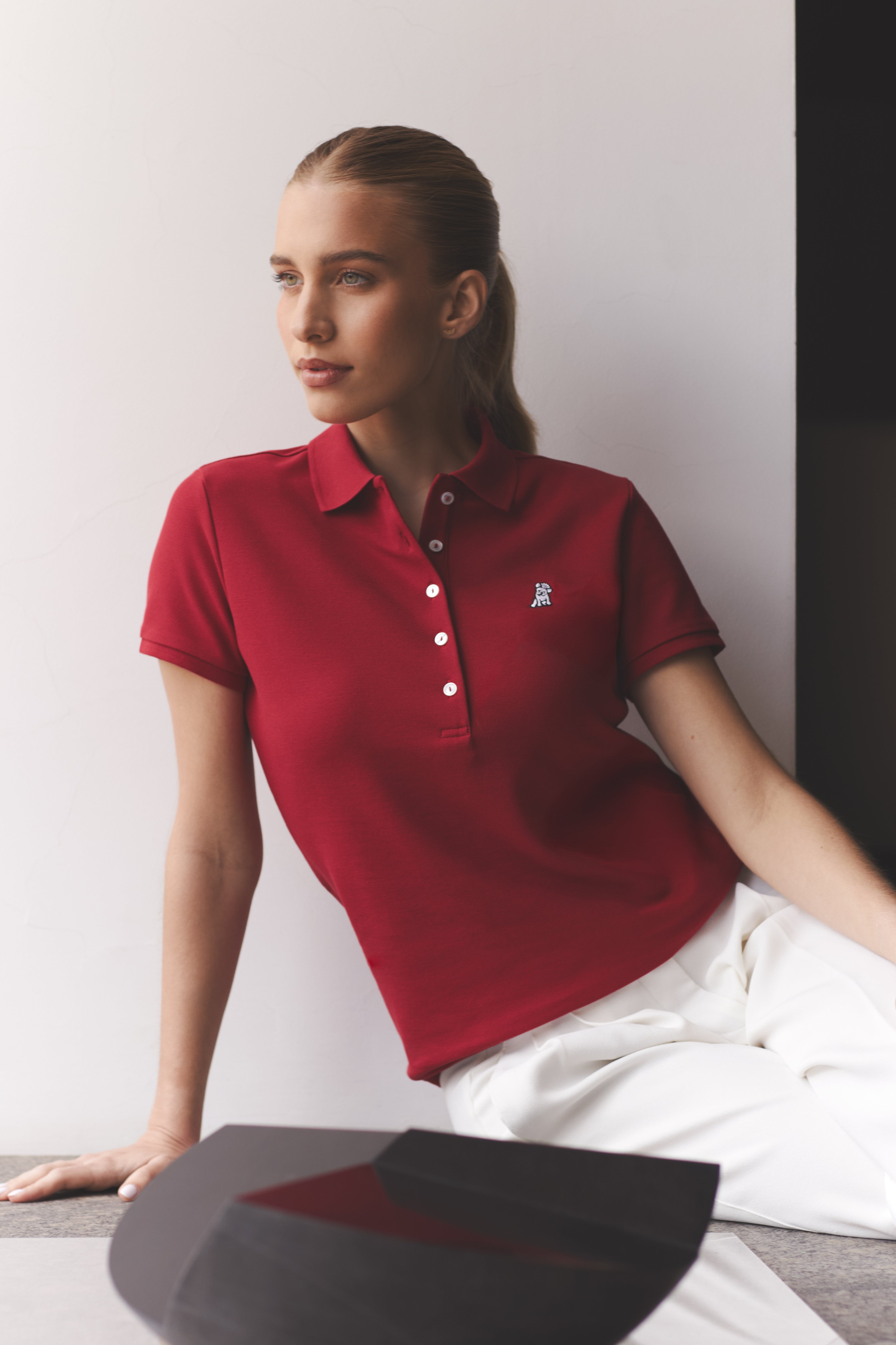 Woman wearing a red polo shirt with a logo, sitting against a plain background