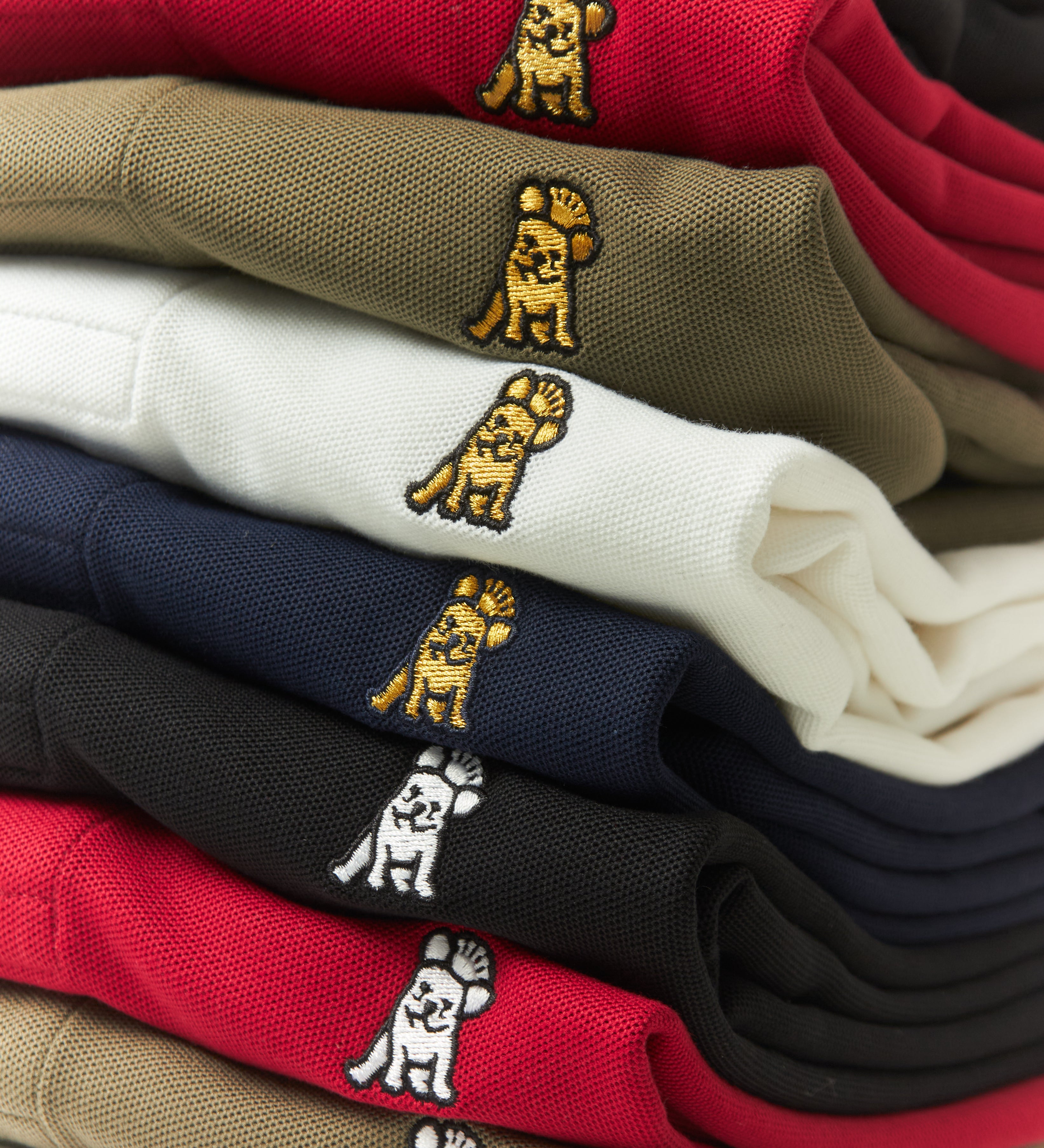Stack of folded shirts with embroidered dog designs on a white background