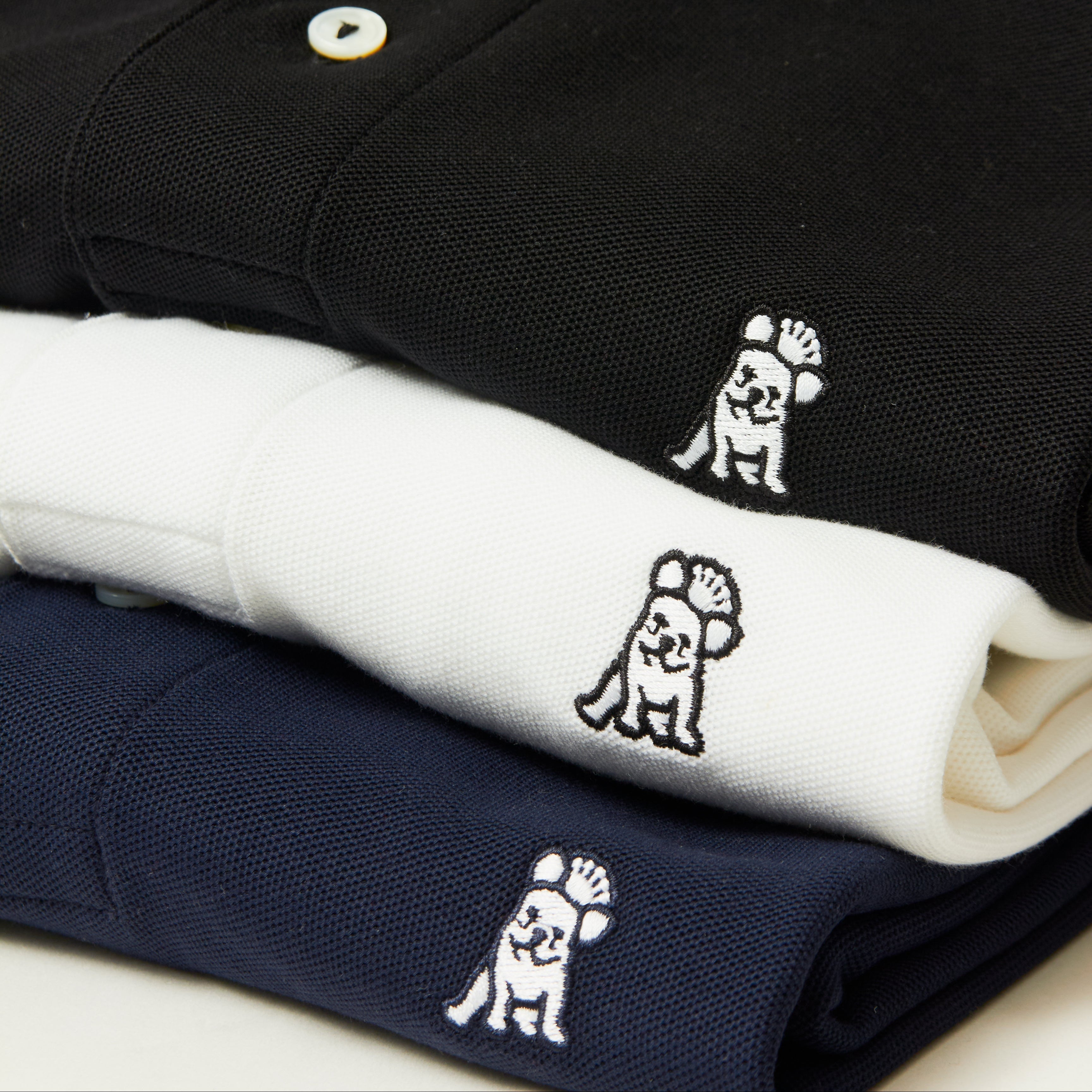 Three folded polo shirts stacked diagonally. Each shirt has a small embroidered dog logo on the chest.