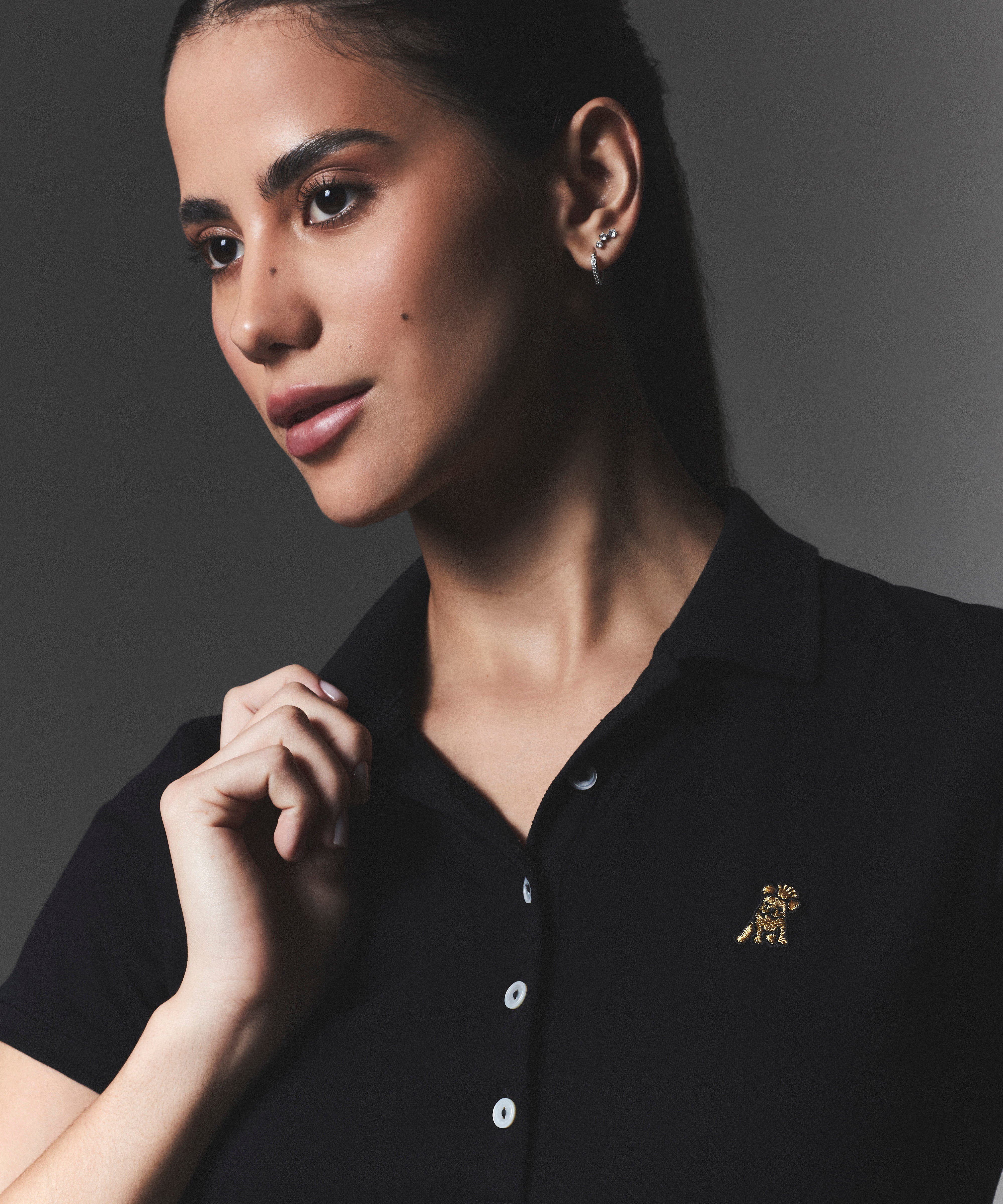 Woman wearing a black polo shirt with a logo on a dark background