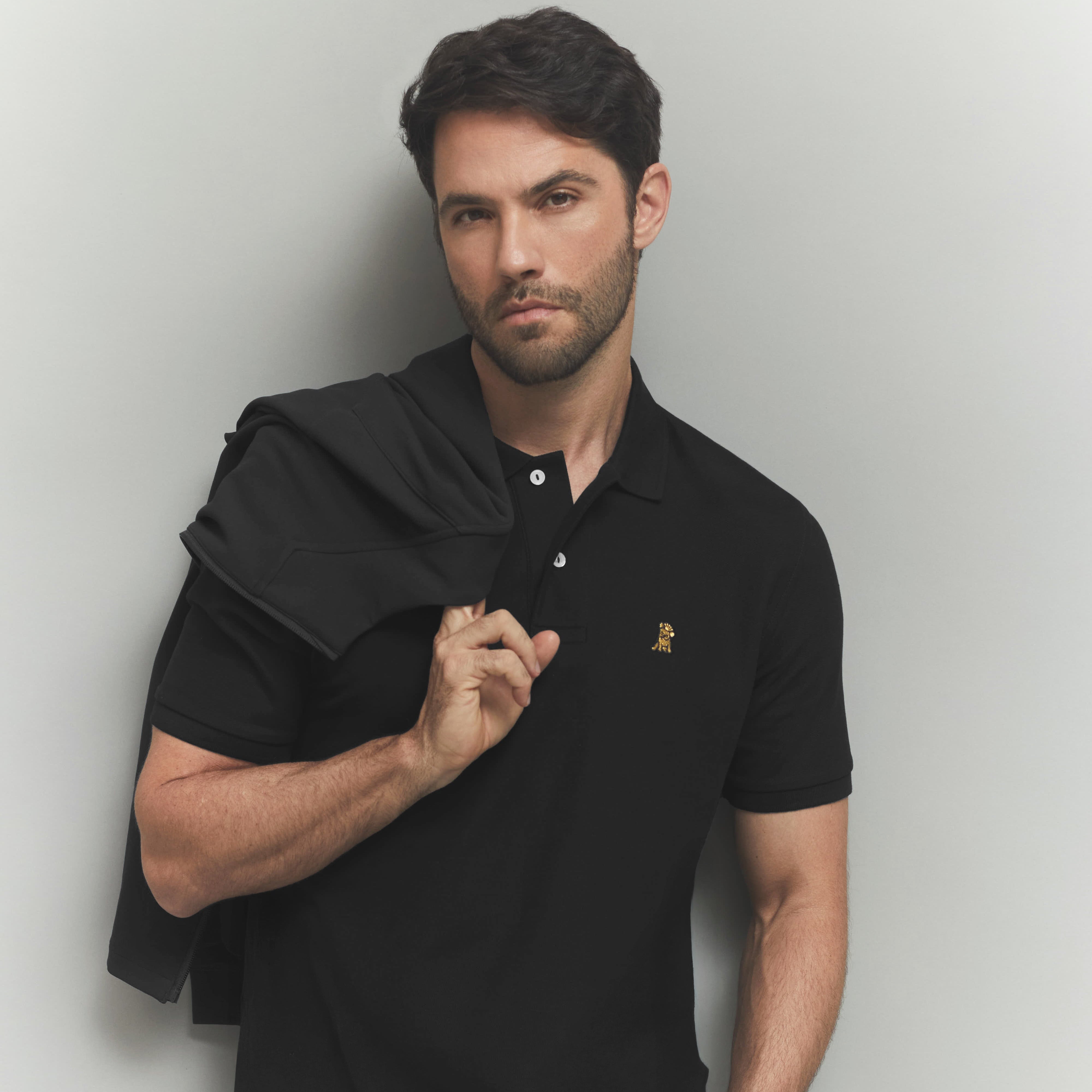 Men wearing a black polo with a gold dog logo on a gray background