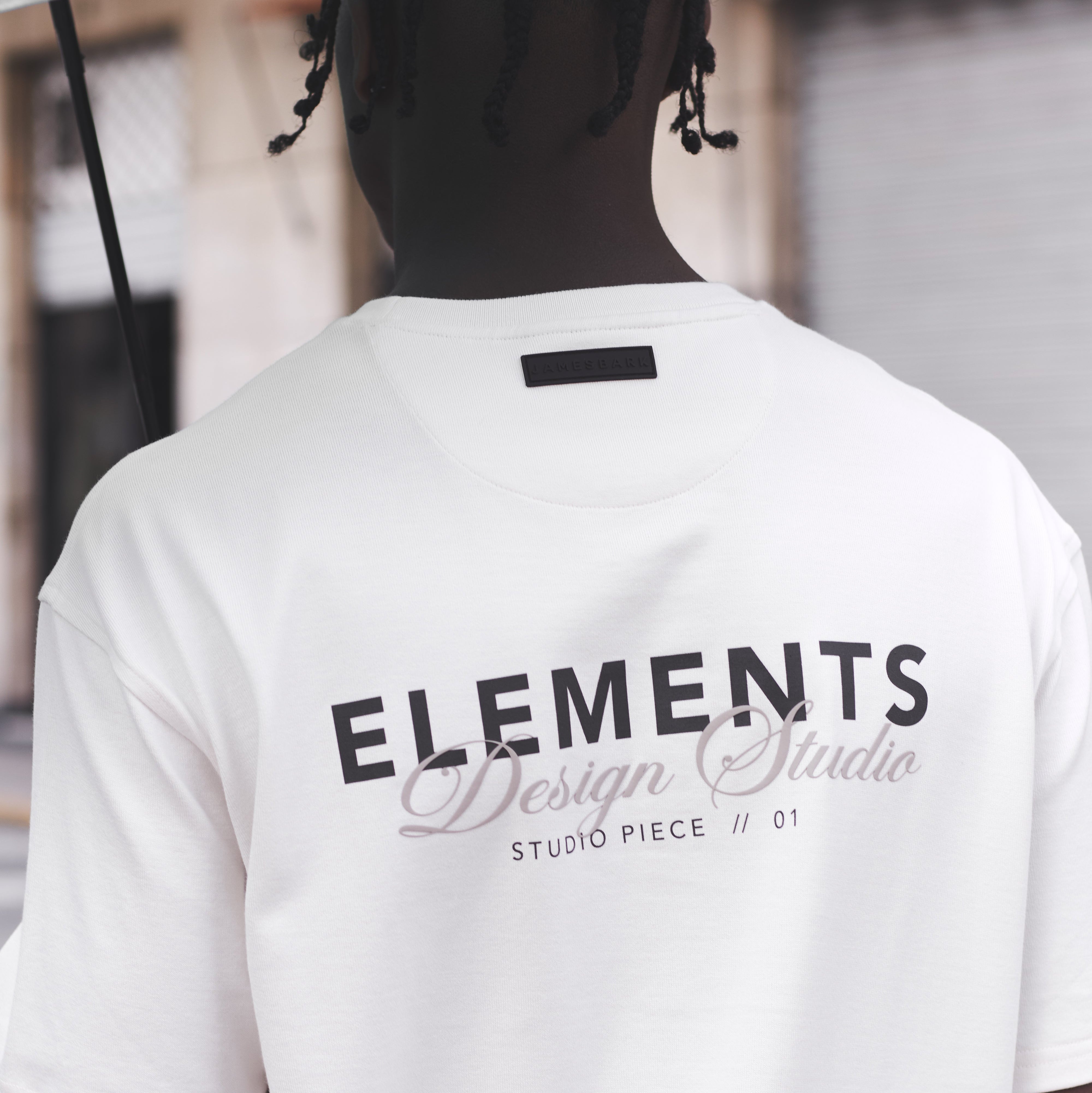 Person wearing a white t-shirt with 'ELEMENTS Design Studio' text on the back.