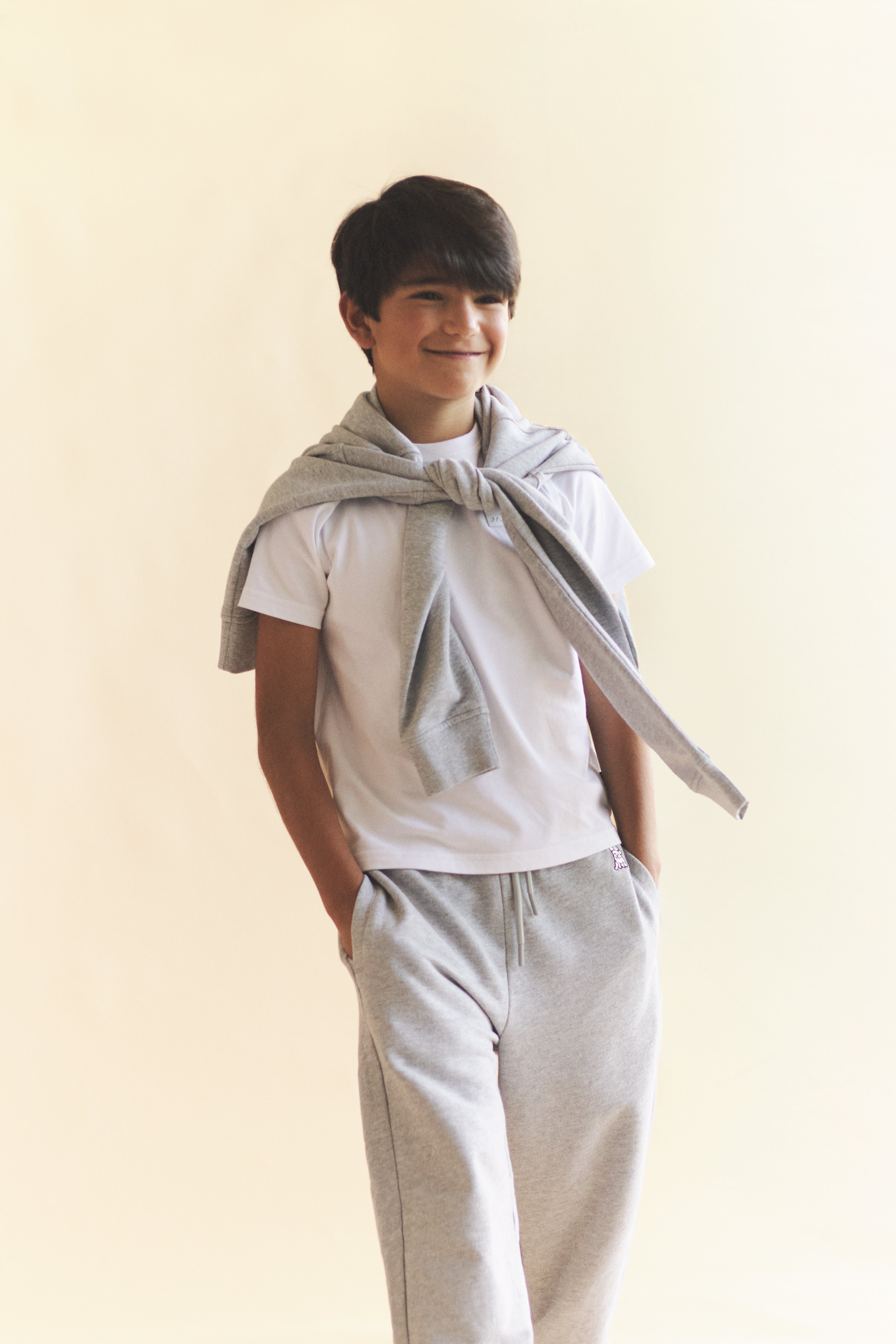 Boy wearing a light gray t-shirt and pants with a matching sweatshirt on a beige background