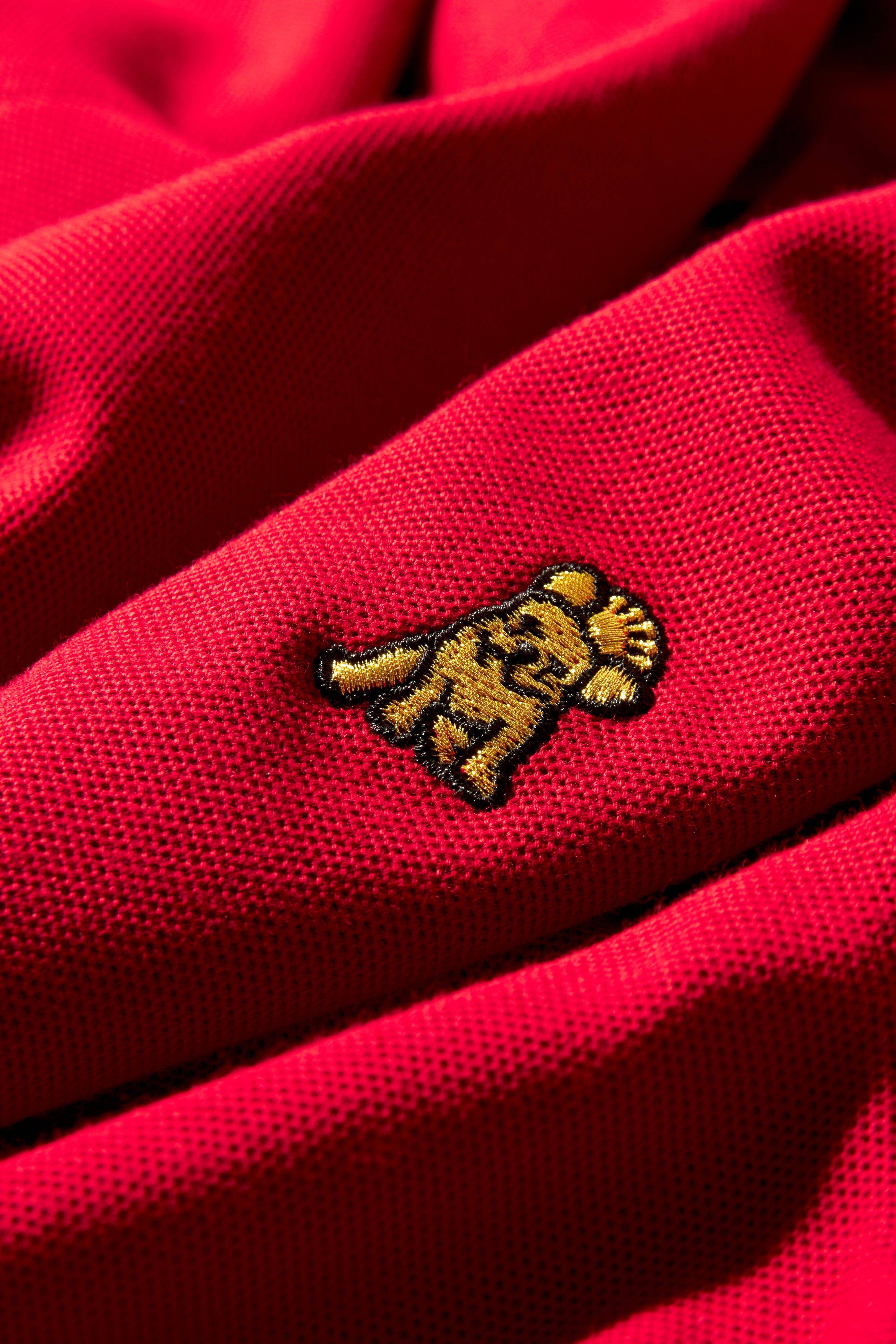 Close-up of a red polo shirt's pique fabric showing a small golden embroidered logo