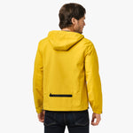 A back view of a bright yellow hooded jacket. The jacket has a clean, minimalist design with a black horizontal zipper pocket at the lower back. The hood is relaxed, and the fit is slightly fitted through the arms and back. The wearer is also shown wearing dark blue jeans, giving a casual and practical appearance.