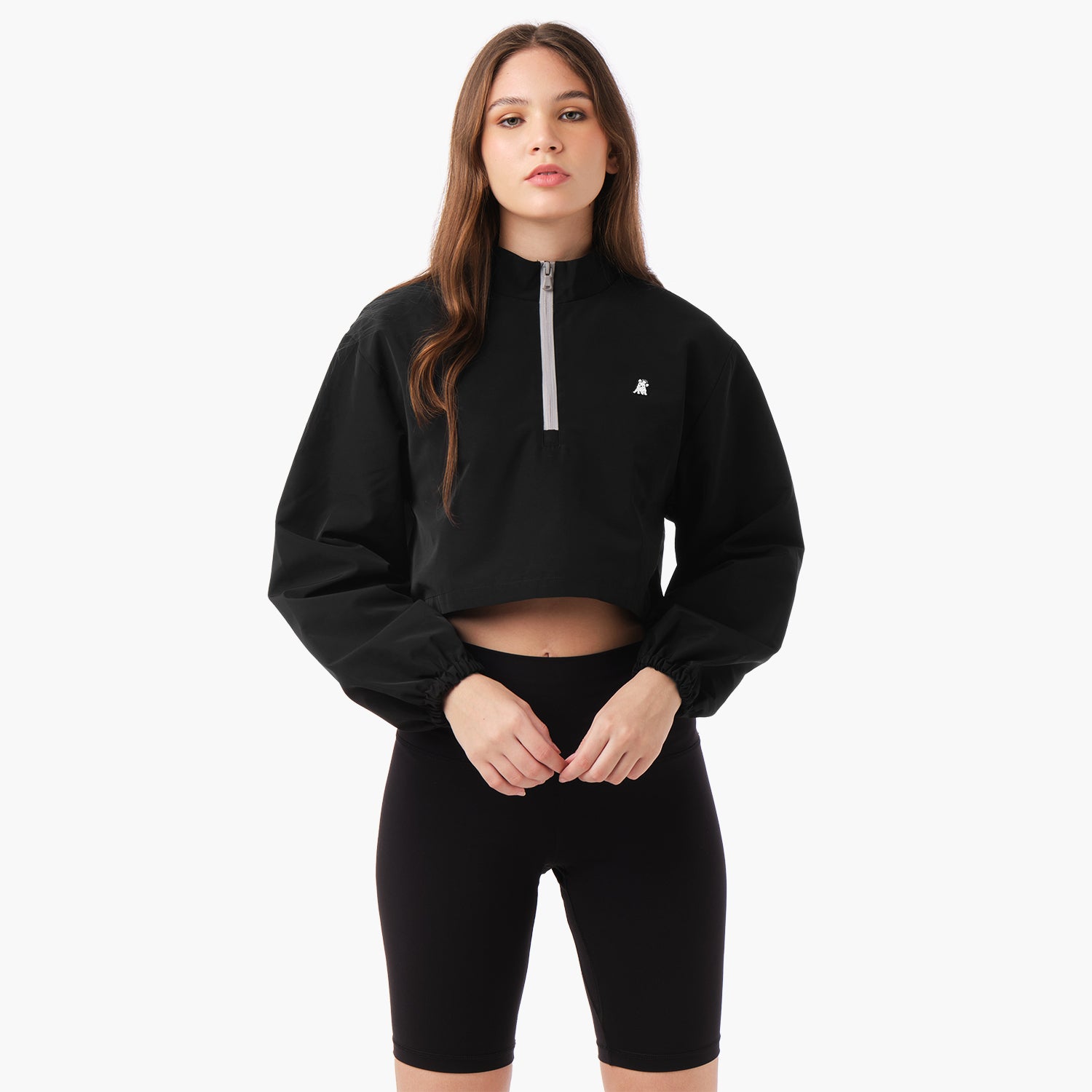 A model wearing a cropped jacket in a black color, styled with sporty shorts. The jacket has a relaxed fit , showcasing a casual look. The model stands in a confident pose against a neutral background.