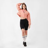 A model poses wearing a cropped jacket and sporty shorts, looking straight to the camera against a neutral background.