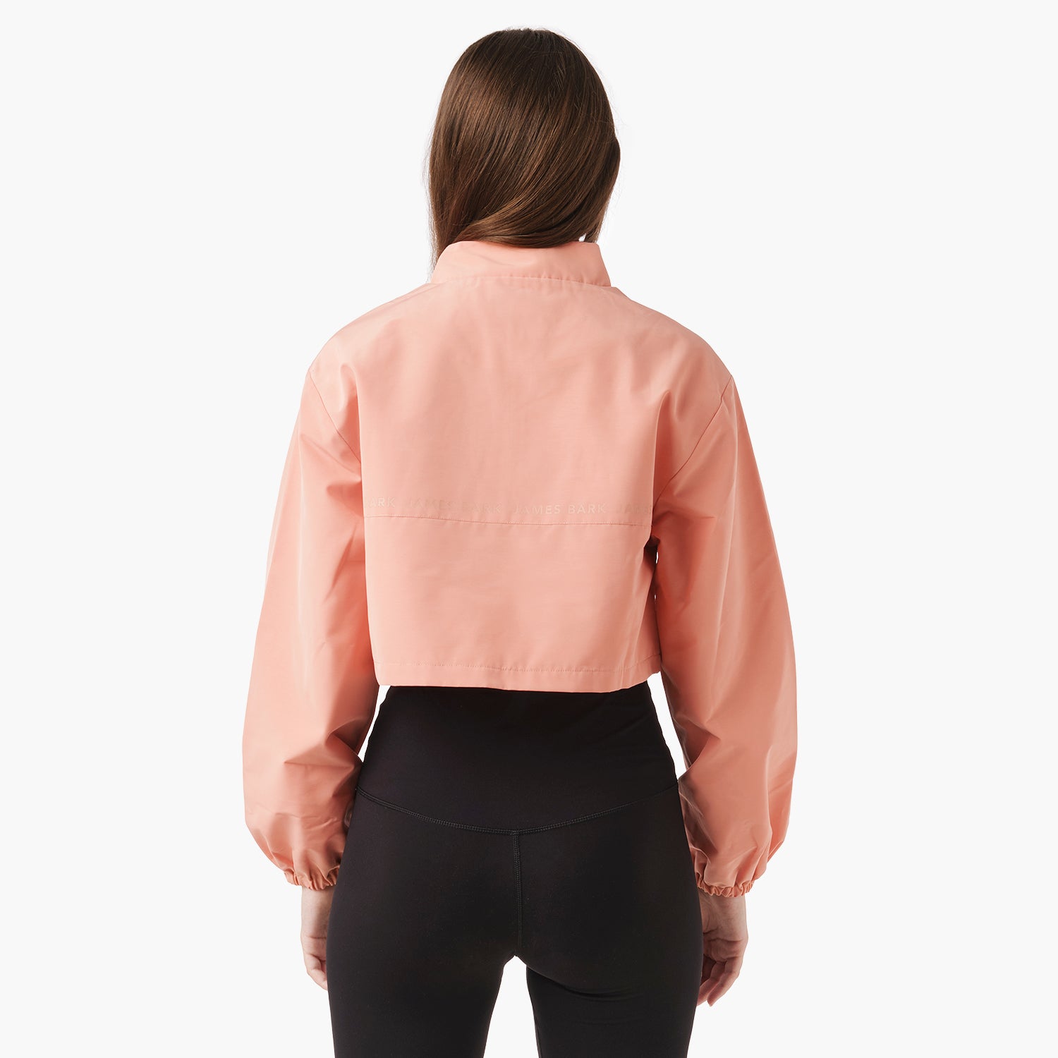 A model poses with her back to the camera, showcasing a beautiful cropped jacket paired with shorts, set against a neutral background.