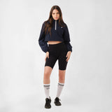 A model poses wearing a cropped jacket and sporty shorts, looking straight to the camera against a neutral background.