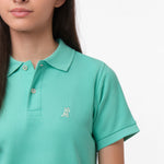 Close-up of the chest area of the mint green polo shirt, featuring the small embroidered logo.