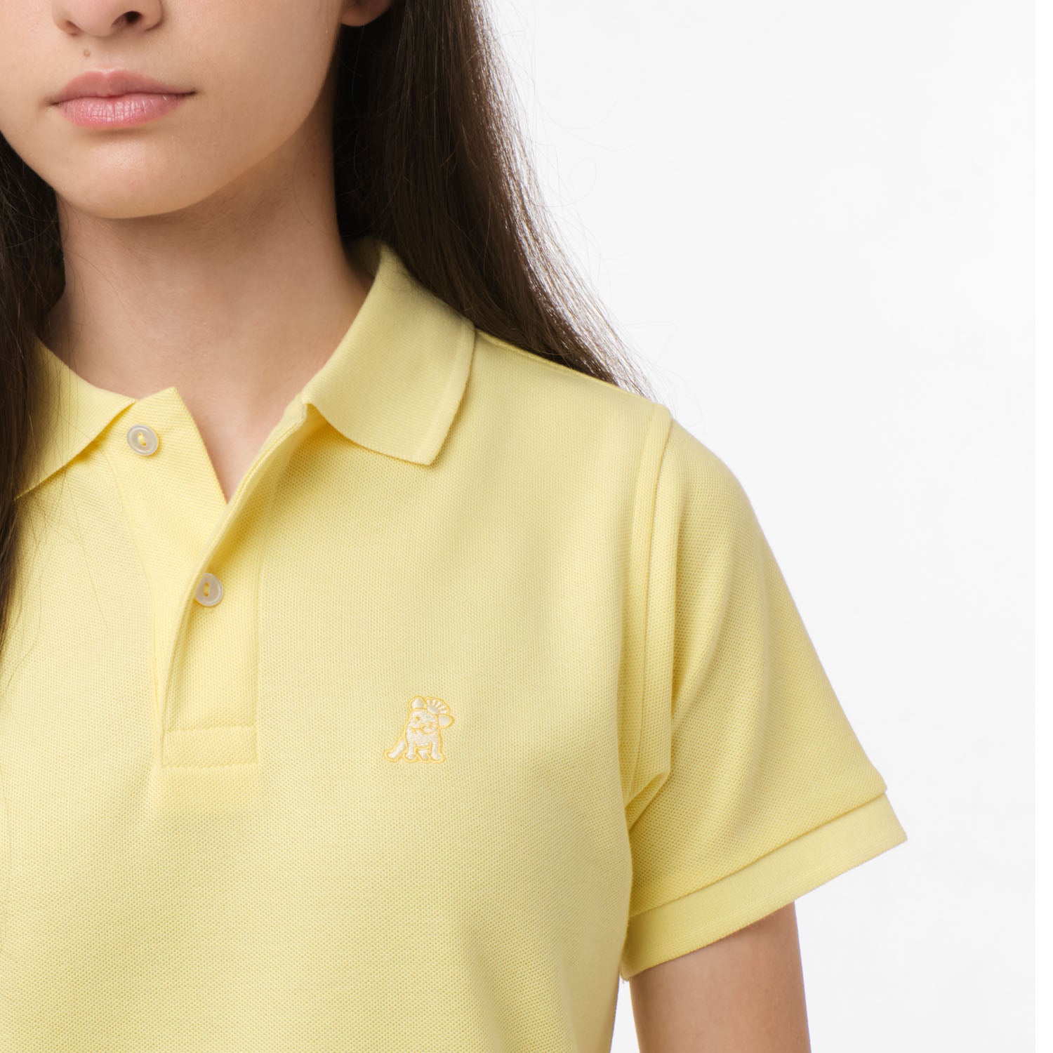 Close-up of the chest area of the yellow polo shirt, featuring the small embroidered logo.