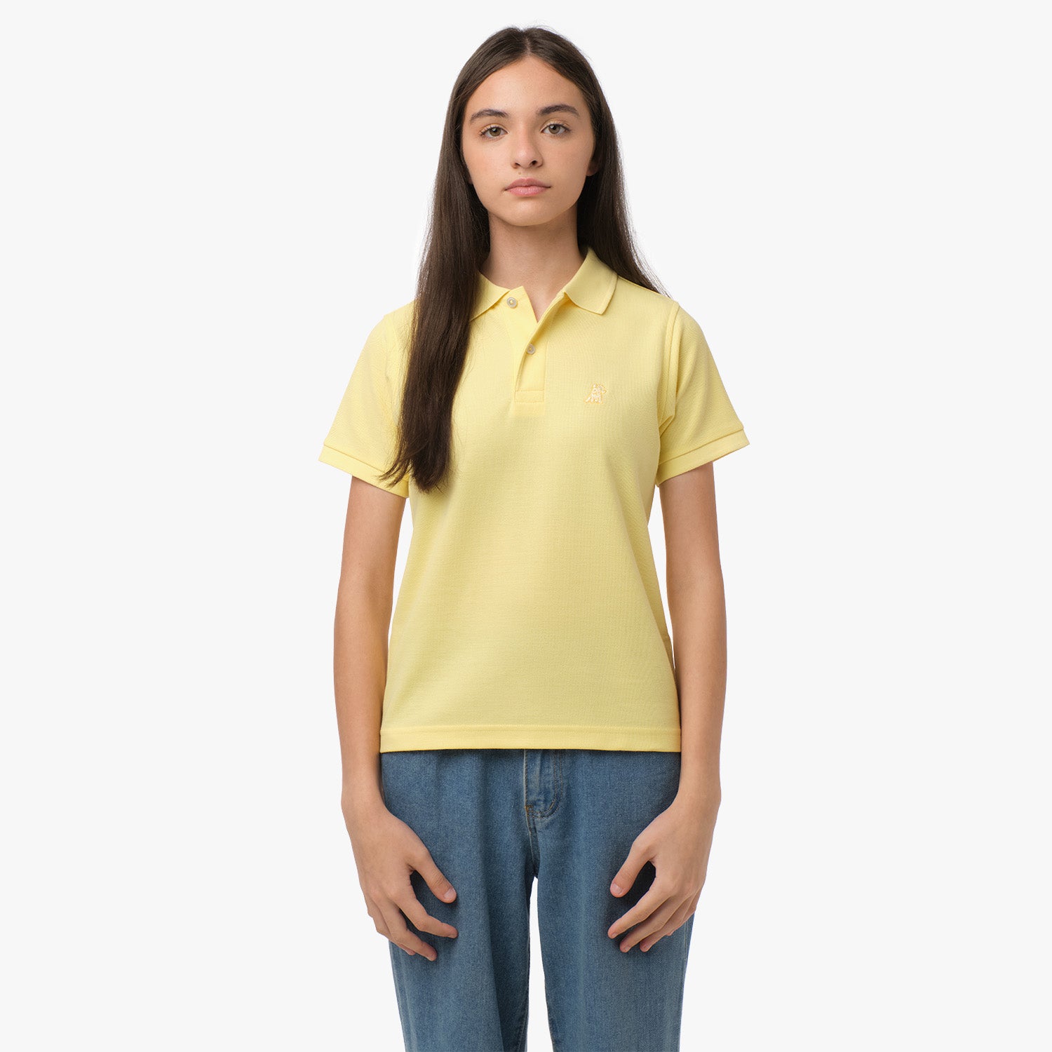 A young woman wearing a yellow polo shirt with a small embroidered logo on the chest, standing with her hands at her sides, paired with blue jeans.