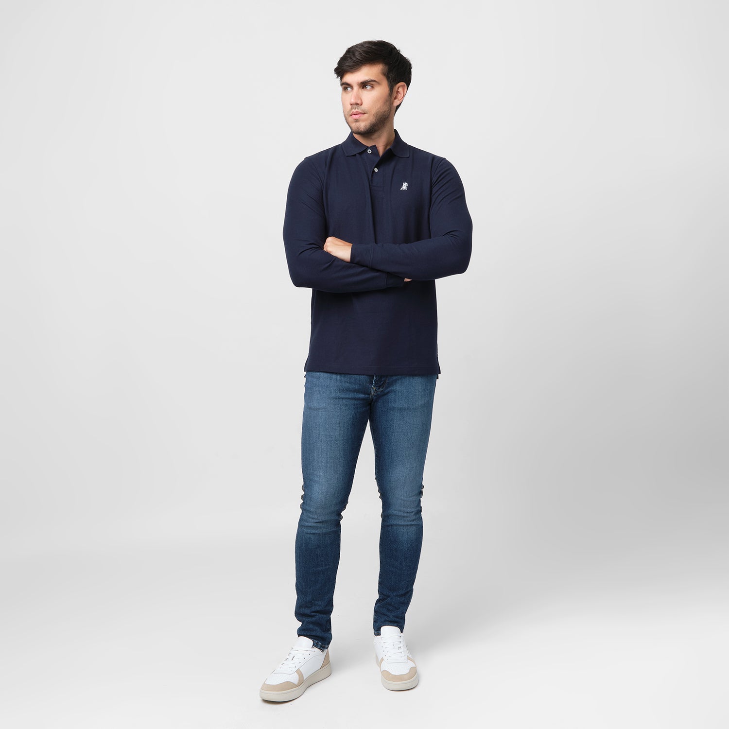 A full-body shot of the man wearing the navy blue long-sleeved polo shirt and blue jeans, standing casually with his arms crossed.