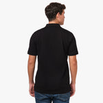 Back view of the black polo shirt worn by a model, highlighting the plain back design.