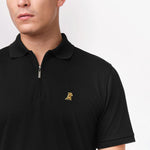 Close-up shot of the collar area of the black polo shirt, showing the gold embroidered logo on the chest.