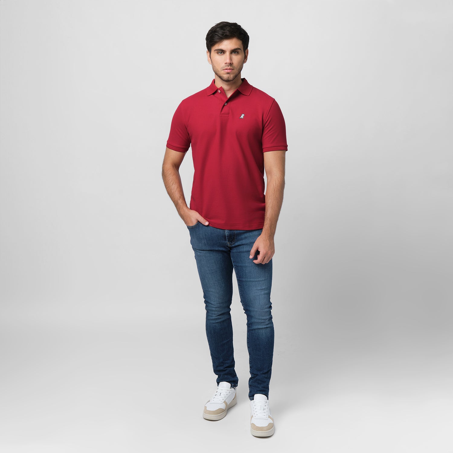 A red polo shirt laid flat, showing the collar and small golden embroidered logo on the chest.