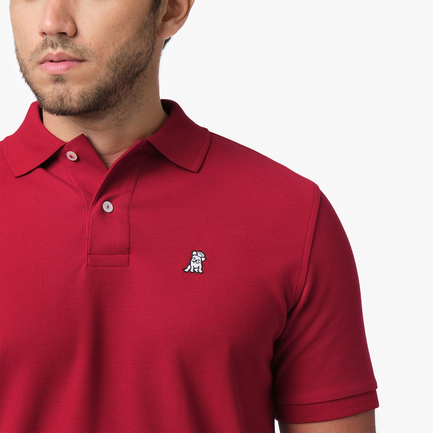 Close-up of a man wearing the red polo shirt, showing the collar and the small golden embroidered logo on the chest.